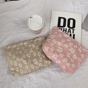 Close-up of beige and pink floral jacquard makeup bags on a white textured background