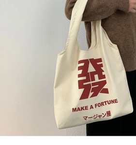 Detail shot of canvas tote bag with red lucky print and text on female shoulder