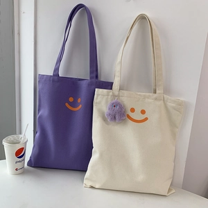 Detail view of purple and white canvas tote bags with orange smiley face and plush pendant