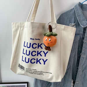 Detail of cute orange plush charm hanging on a white canvas tote bag with blue lucky text