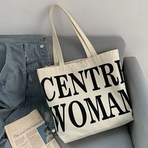 Minimalist beige canvas tote bag with black lettering placed on a grey sofa