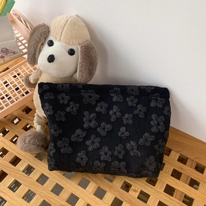 Detail of black jacquard cosmetic bag with embossed floral texture on wooden stand