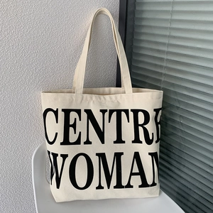 Detailed view of cream canvas tote bag with black CENTRE WOMAN lettering on a chair