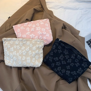 Close-up of floral embroidered cosmetic bags in pink, white, and black with 3D texture