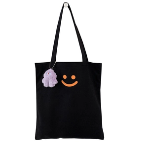 Minimalist black canvas tote bag with orange smiley face and purple plush monster charm
