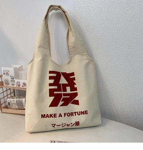 Close-up of cream canvas tote bag with red Make A Fortune text and linen texture detail