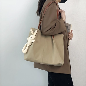 Detail of khaki nylon tote bag with leather straps and cute bunny plush charm accessory
