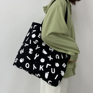 Close-up of a large black canvas tote bag with white letter patterns worn by a model