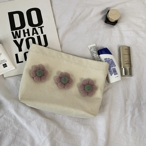 Detailed close-up of a cream canvas makeup bag with 3D floral accents and skincare props