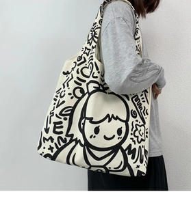 Detailed shot of large cream canvas tote bag with black artistic doodle prints on model