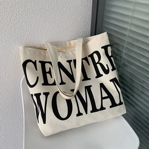 Detail of minimalist canvas tote bag with black large CENTRE WOMAN lettering on white chair