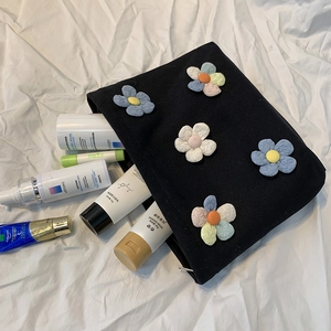 Black canvas cosmetic bag with colorful 3D flower patches and skincare items display
