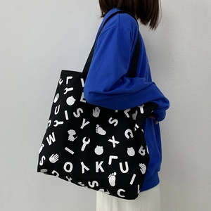 Detail of black canvas tote bag with white letter print worn over the shoulder