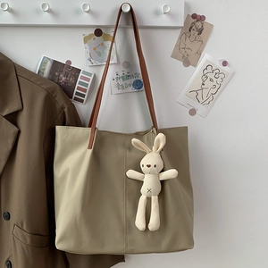 Detail of khaki nylon tote bag with brown straps and cute white bunny plush pendant