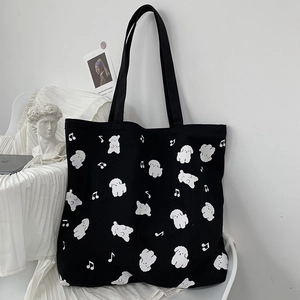 Gros plan d'un sac cabas en toile noire avec motifs chiens blancs sur une chaise blanche