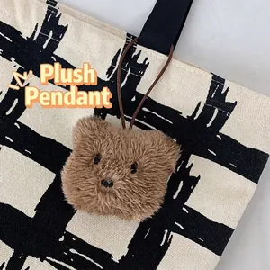 Brown plush bear pendant hanging on a minimalist checkered canvas tote bag