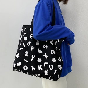 Detail of a large black canvas tote bag with white graphic prints worn with a blue hoodie