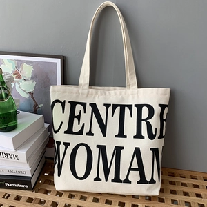 Detailed view of off-white canvas tote with large black lettering on wood bench