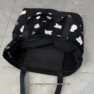 Détail du sac cabas en toile noire montrant la fermeture éclair et la poche intérieure