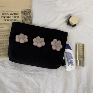 Detail of black canvas cosmetic bag featuring three pink plush flowers with zip closure