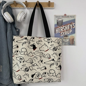 Detail of canvas tote bag featuring dog prints and black handles on a wooden hook