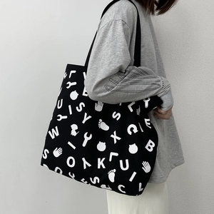 Close-up of a large black canvas tote bag with white graphic letter prints on a shoulder
