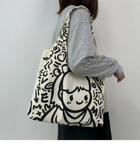 Detail view of large canvas tote bag with black cartoon graffiti and wide shoulder strap