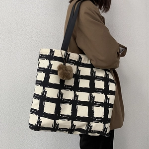 Canvas tote bag with black grid pattern and plush charm shown on person's shoulder