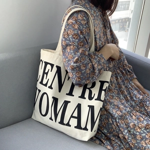 Detail of white canvas tote bag with black letter print shown in a lifestyle setting