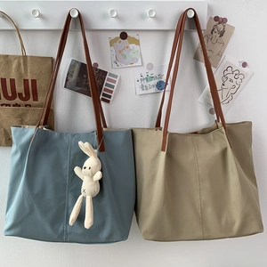 Detail of grey-blue and khaki nylon tote bags with bunny charm on white wooden hooks