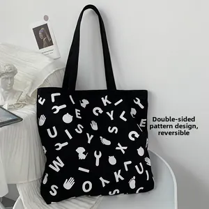 Detail of a large black canvas tote bag with white graphic prints and dual shoulder straps