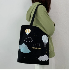 Detail of a large black canvas tote bag with a colorful hot air balloon print on a model