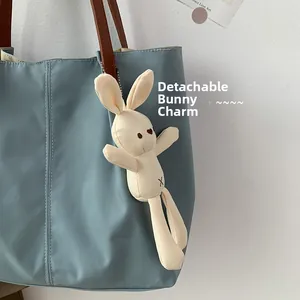 Detail of blue canvas tote bag with brown straps and detachable bunny charm accessory