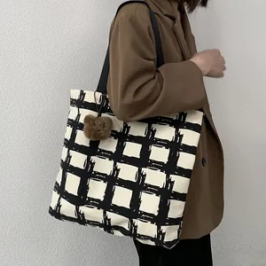 Detail of checkered canvas tote bag featuring brown plush bear charm and sturdy black straps
