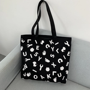 Detailed view of black canvas tote bag with white graphic prints on a light sofa
