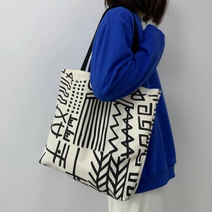 Detail of artistic canvas tote bag with black geometric patterns and webbed shoulder straps