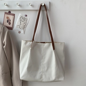 Minimalist cream tote bag hanging on a hook with brown shoulder straps and middle seam detail