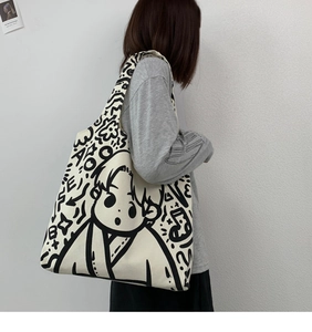 Detail of a large canvas tote bag featuring black hand-drawn cartoon graffiti on white cloth