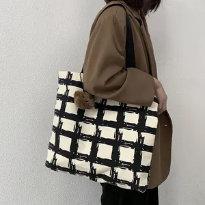 Detail of checkered canvas tote bag with decorative plush ball charm on shoulder