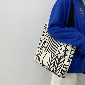 Detail of white canvas tote bag with black abstract geometric patterns and broad shoulder strap