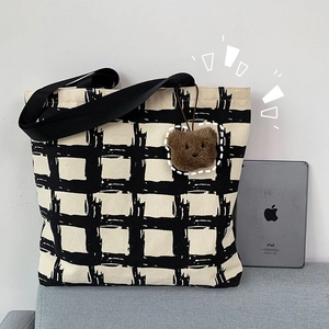 Detail of checkered canvas tote bag with black shoulder strap and brown plush bear charm