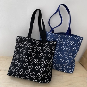 Close-up of black and navy canvas tote bags featuring a white heart pattern print