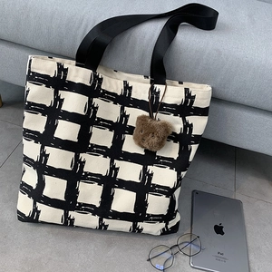 Large canvas tote bag with black grid pattern, shoulder straps, and brown bear pendant