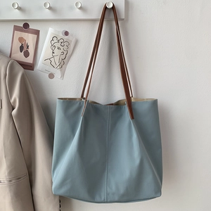 Close-up of light blue nylon tote bag with brown leather straps hanging on a wall