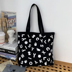 Detail view of a black canvas tote bag with white artistic graffiti print on a desk