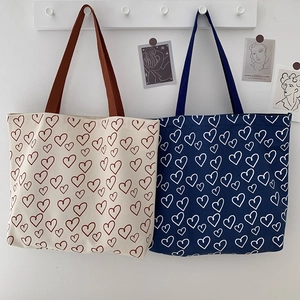 Detail of canvas tote bags with heart patterns hanging on a wooden wall hook