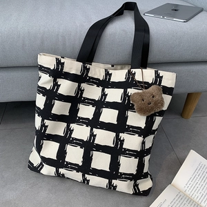 Detail of checkered canvas tote bag with brown bear charm and black woven handles