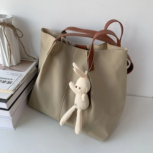 Detail of khaki nylon tote bag featuring a cute white bunny plush pendant and brown handles