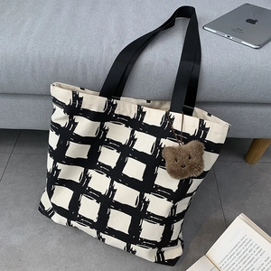 Detail of checkered canvas tote bag with a brown plush bear keychain and sturdy straps