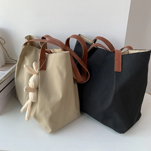 Detail of minimalist nylon tote bags with brown leather handles and rabbit plush pendant